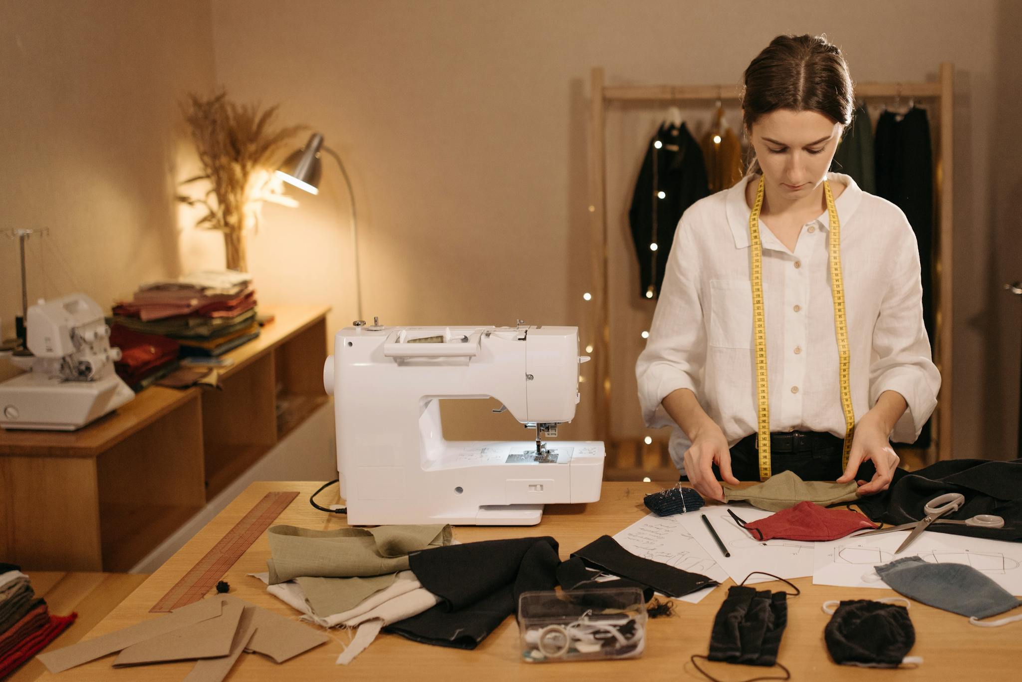 A woman tailor sewing in a studio with fabric, scissors, and a sewing machine.