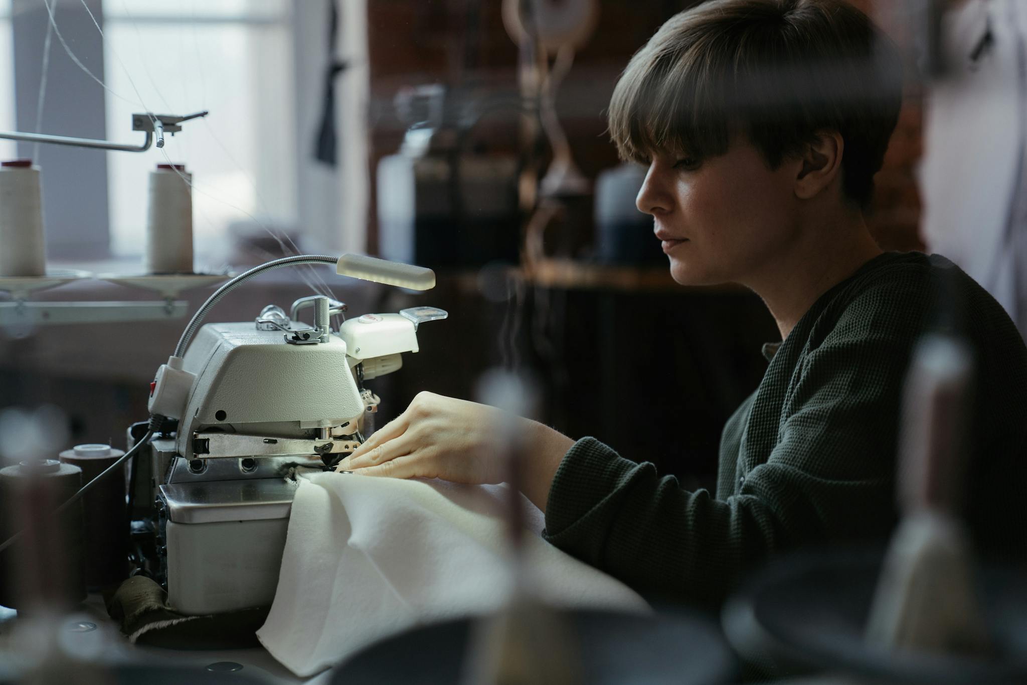 Woman using an overlock machine in a sewing workshop, showcasing concentration and craftsmanship.